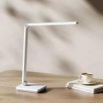 چراغ مطالعه شیائومی Mijia Desk Lamp 2 Lite با طراحی مینیمال و بازوی قابل‌تنظیم روی میز کار در کنار کتاب‌ها و فنجان