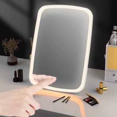 آینه آرایشی شیائومی مدل NV026 با طراحی مستطیلی و نور LED یکپارچه، مجهز به دکمه لمسی در بخش پایینی، قرارگرفته روی میز آرایشی همراه با لوازم آرایش و دکوراسیون پس‌زمینه